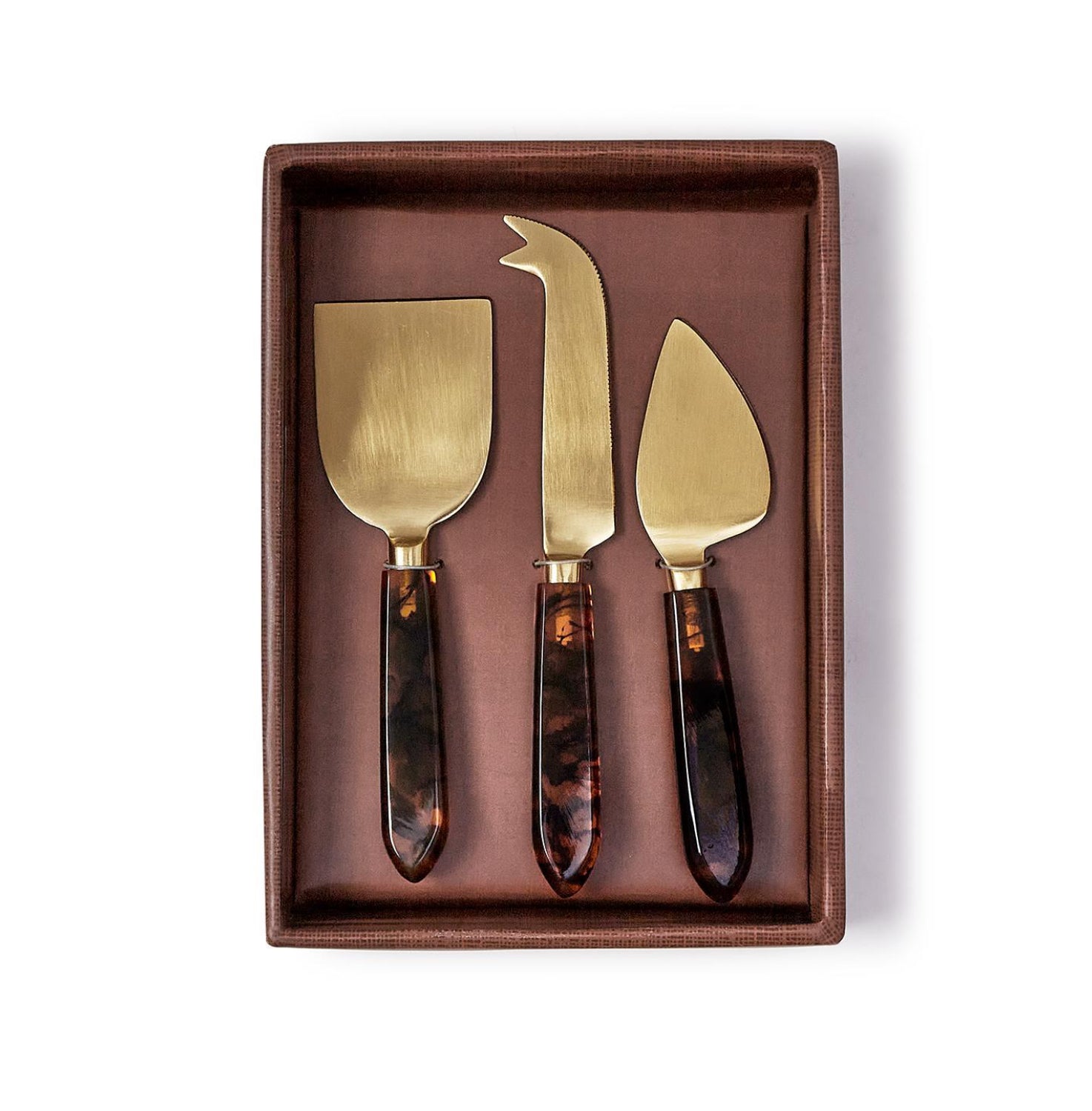 Set of three gold cheese knives with tortoiseshell handles in a brown box on a white background