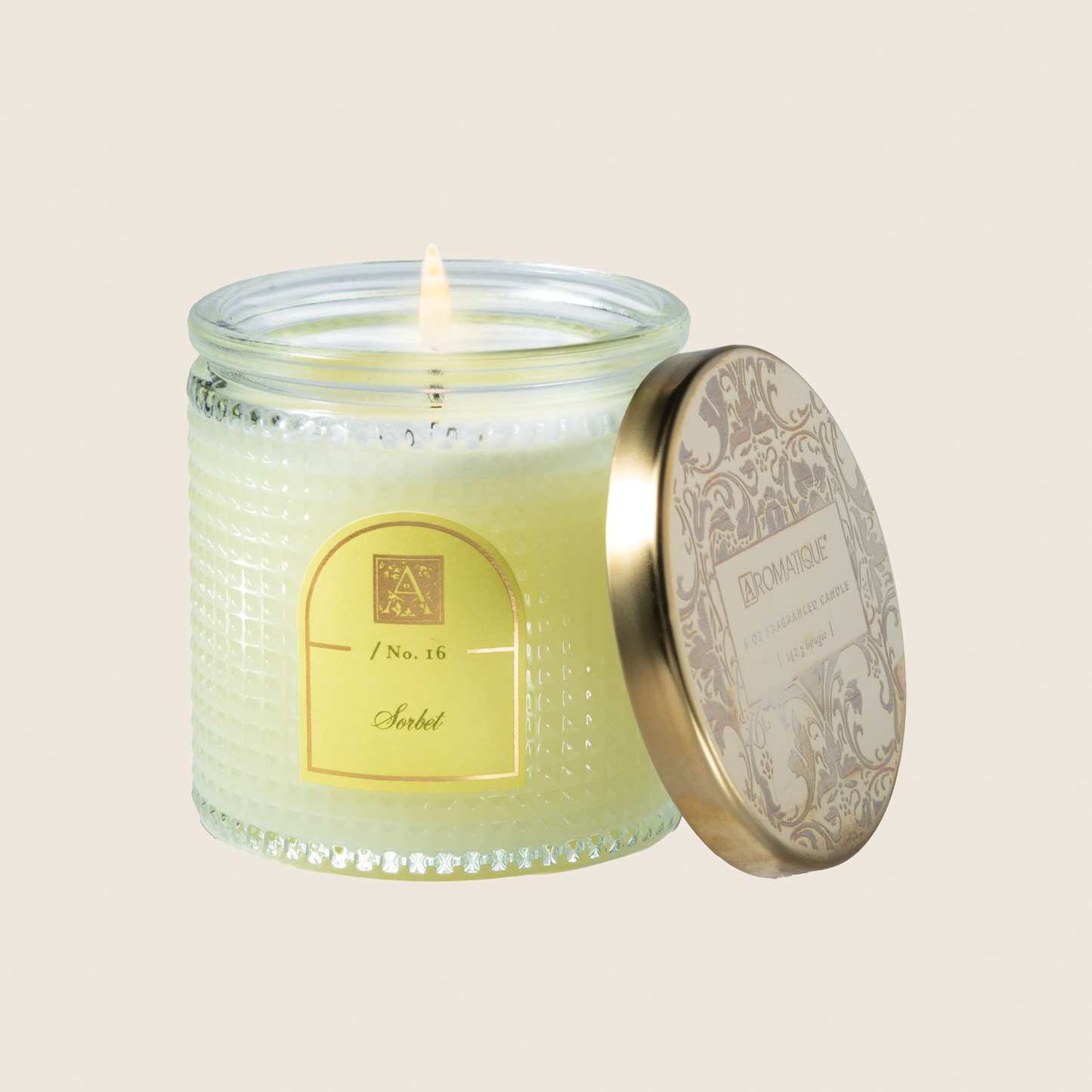 Glass candle with decorative label and lid on a beige background