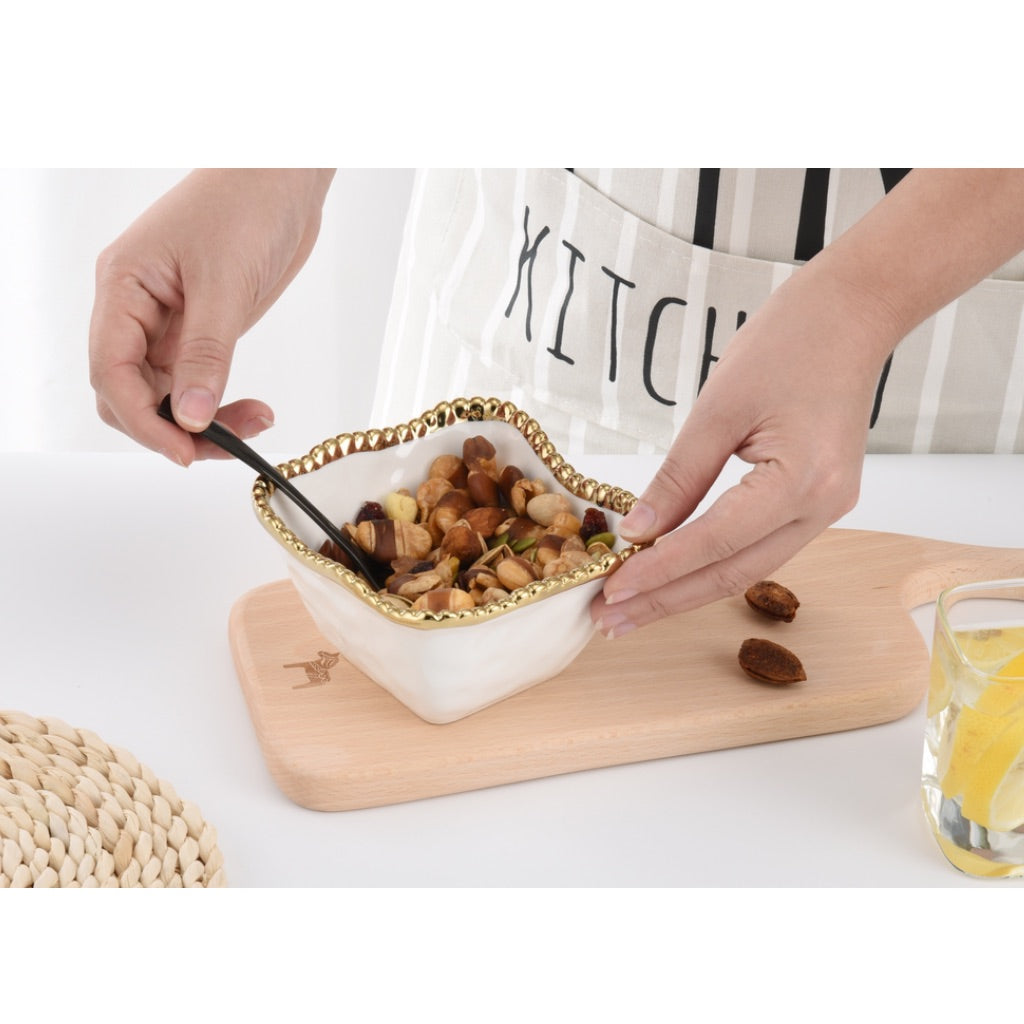 Person holding a white bowl with gold rim filled with nuts on a wooden board.