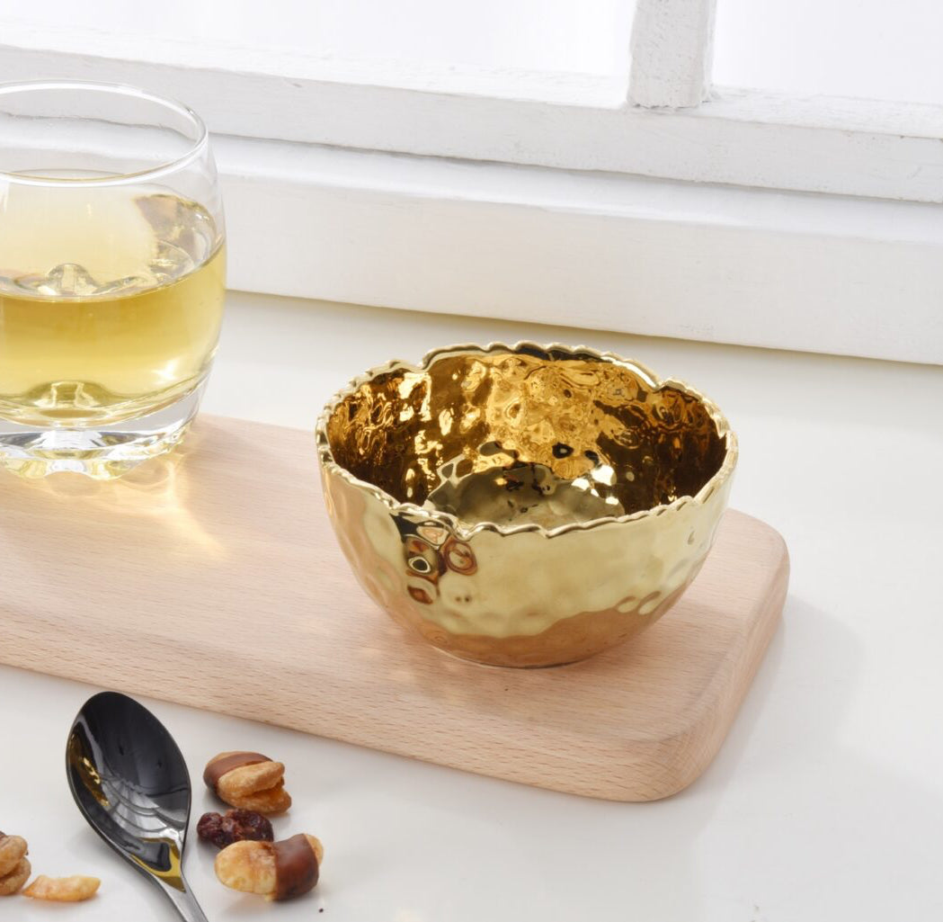 Gold bowl on a wooden board with a glass of yellow liquid and a spoon.