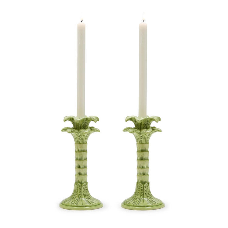 Two green palm tree candlestick holders with white candles on a white background.