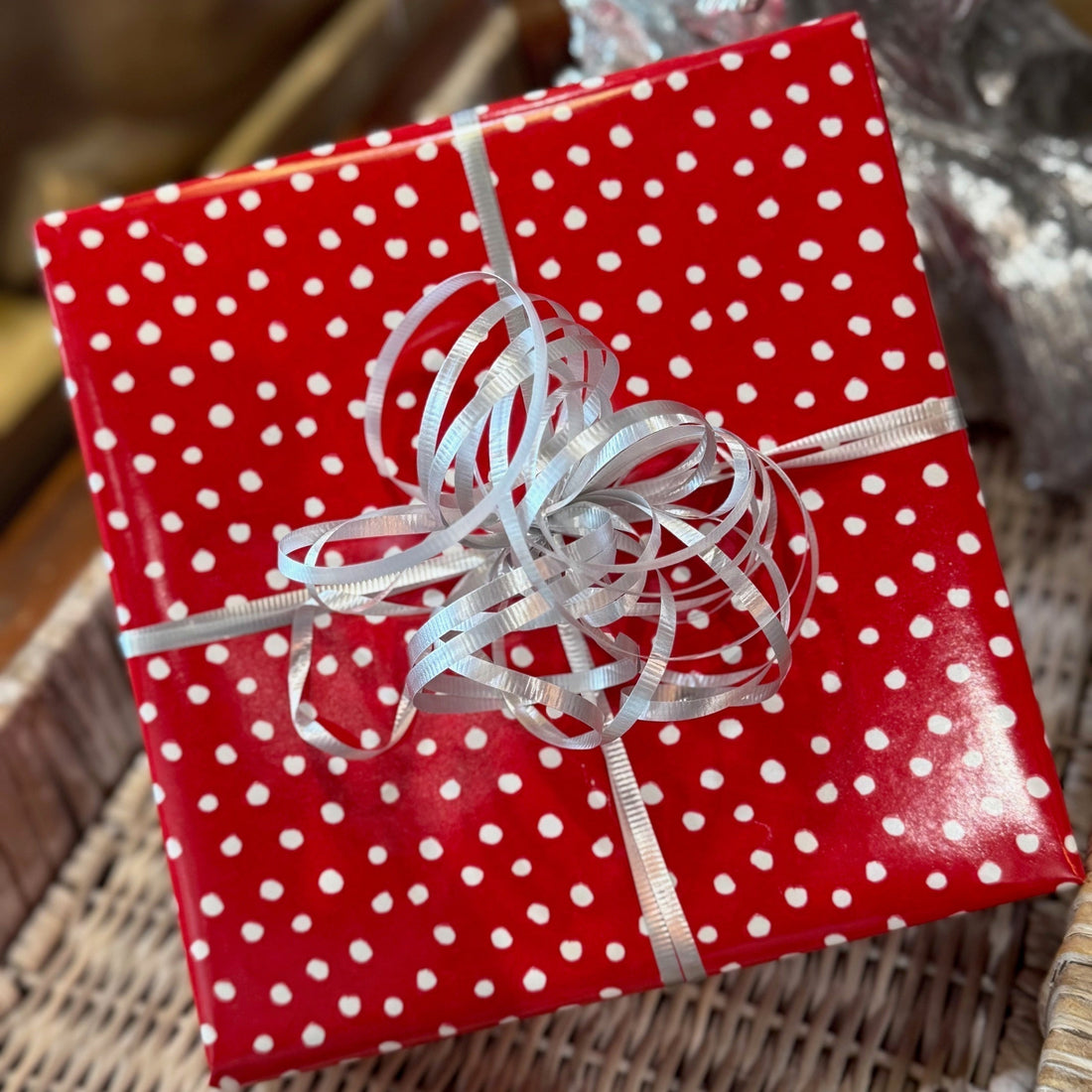 A wrapped present in red paper with white dots and a frilly silver ribbon