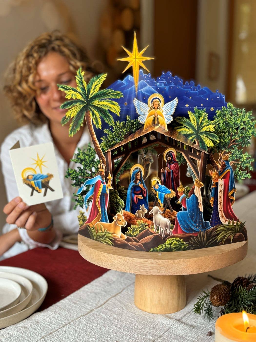Nativity scene pop-up card on a wooden stand with a woman holding a card in the background
