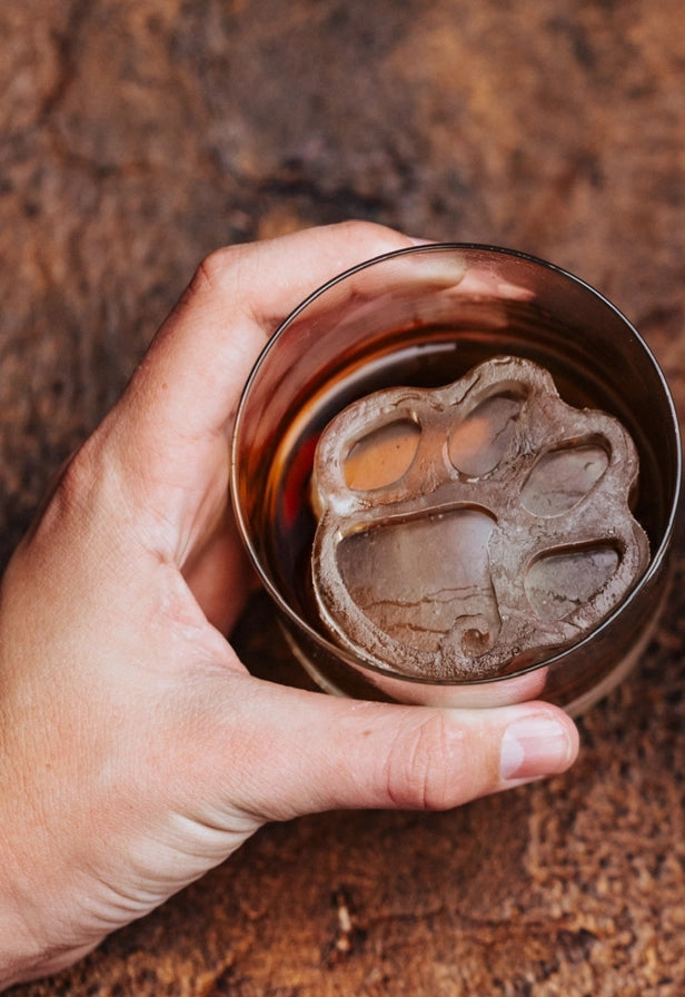 Hand holding a glass with a paw print design on a wooden surface