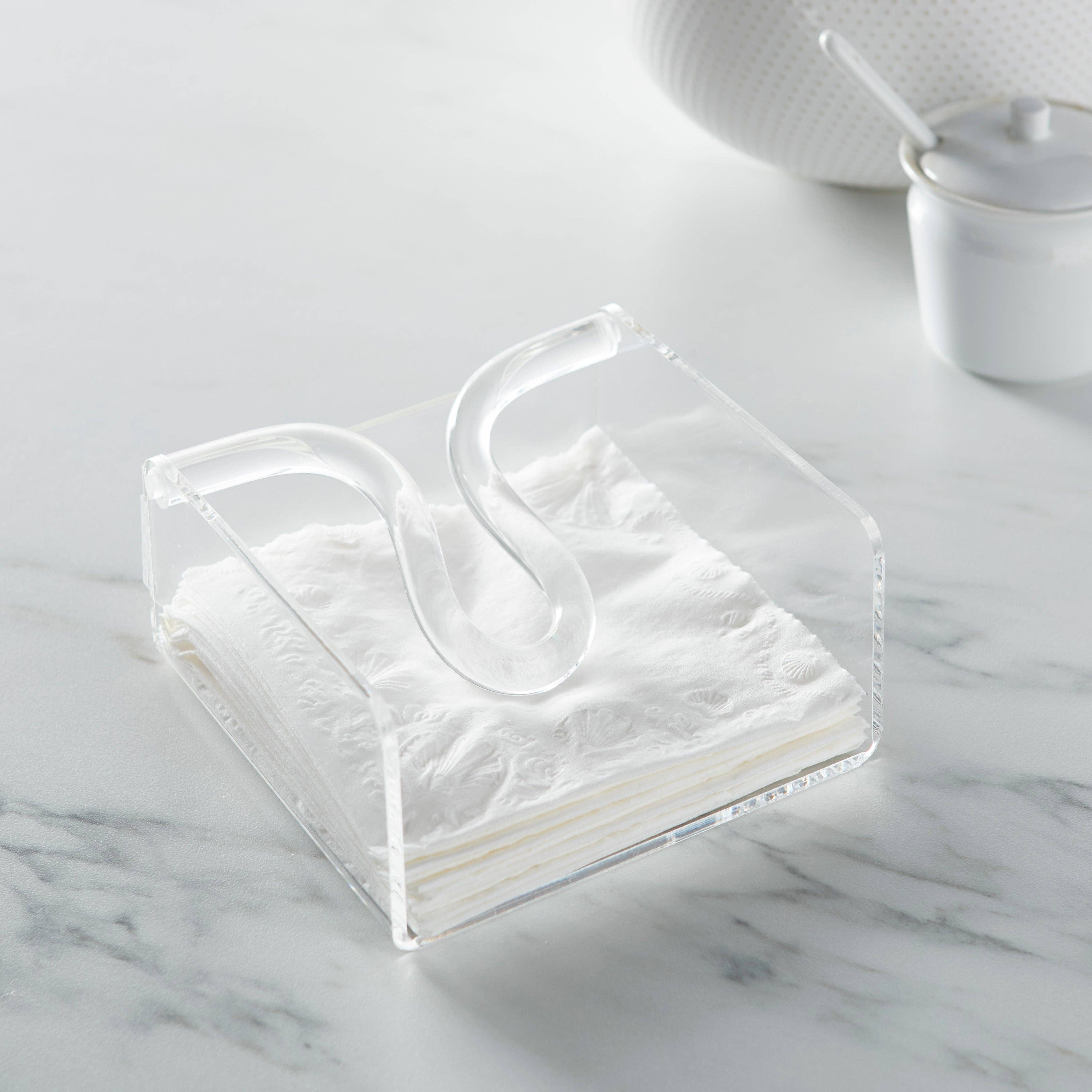 Huang Acrylic brand Clear acrylic square cocktail napkin holder with bow rod filled with white napkins placed on a light marble surface with softly blurred white ceramic dishes in the background.