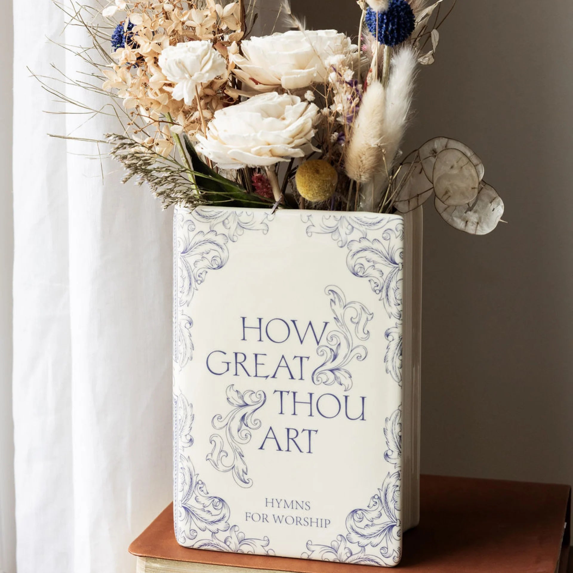 Vase with flowers on top of a hymn book titled 'How Great Thou Art'.