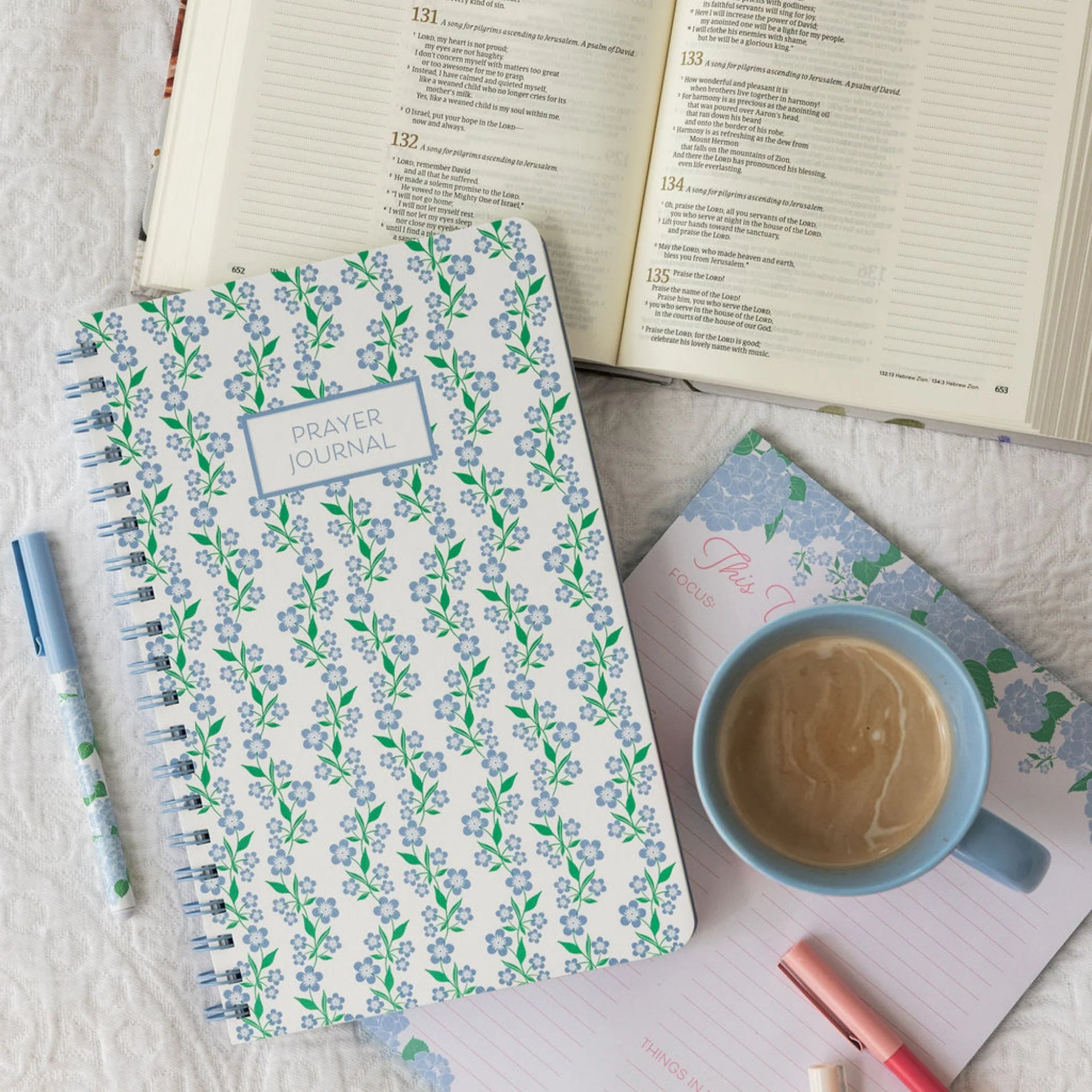Floral-patterned prayer journal with a cup of coffee and pens on a textured surface