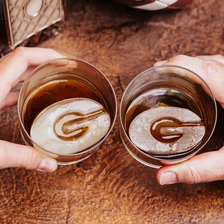 Two hands holding glasses of coffee with latte art on a wooden surface