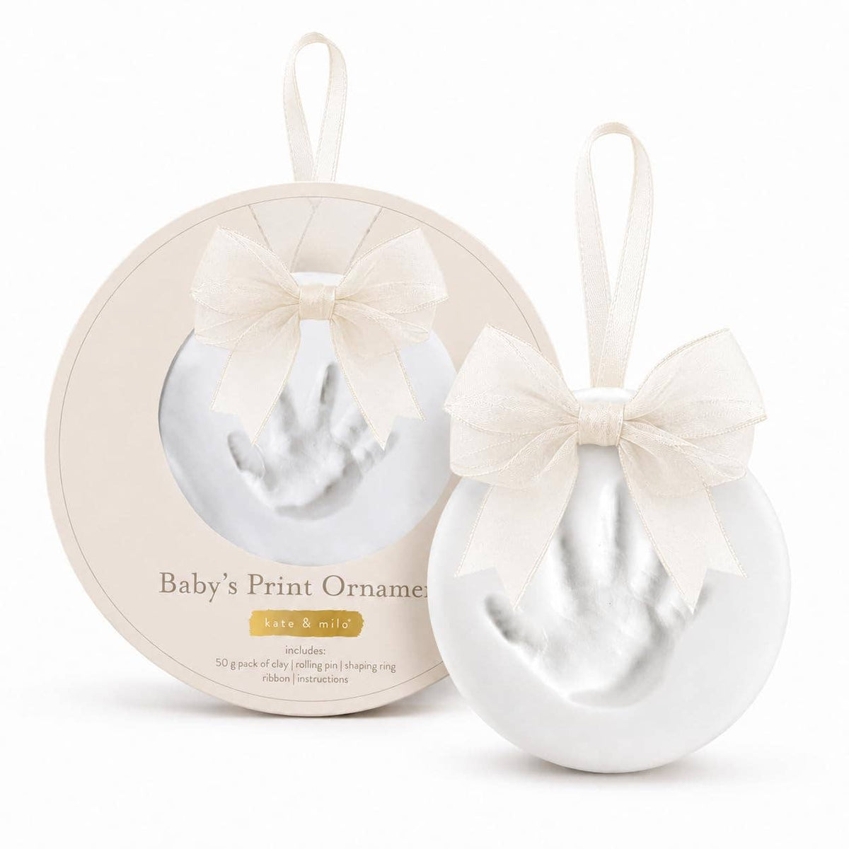 A baby's print ornament set featuring a round white ornament with a white fabric bow and hanging loop, next to its circular beige packaging box with a clear window showing the white print inside.