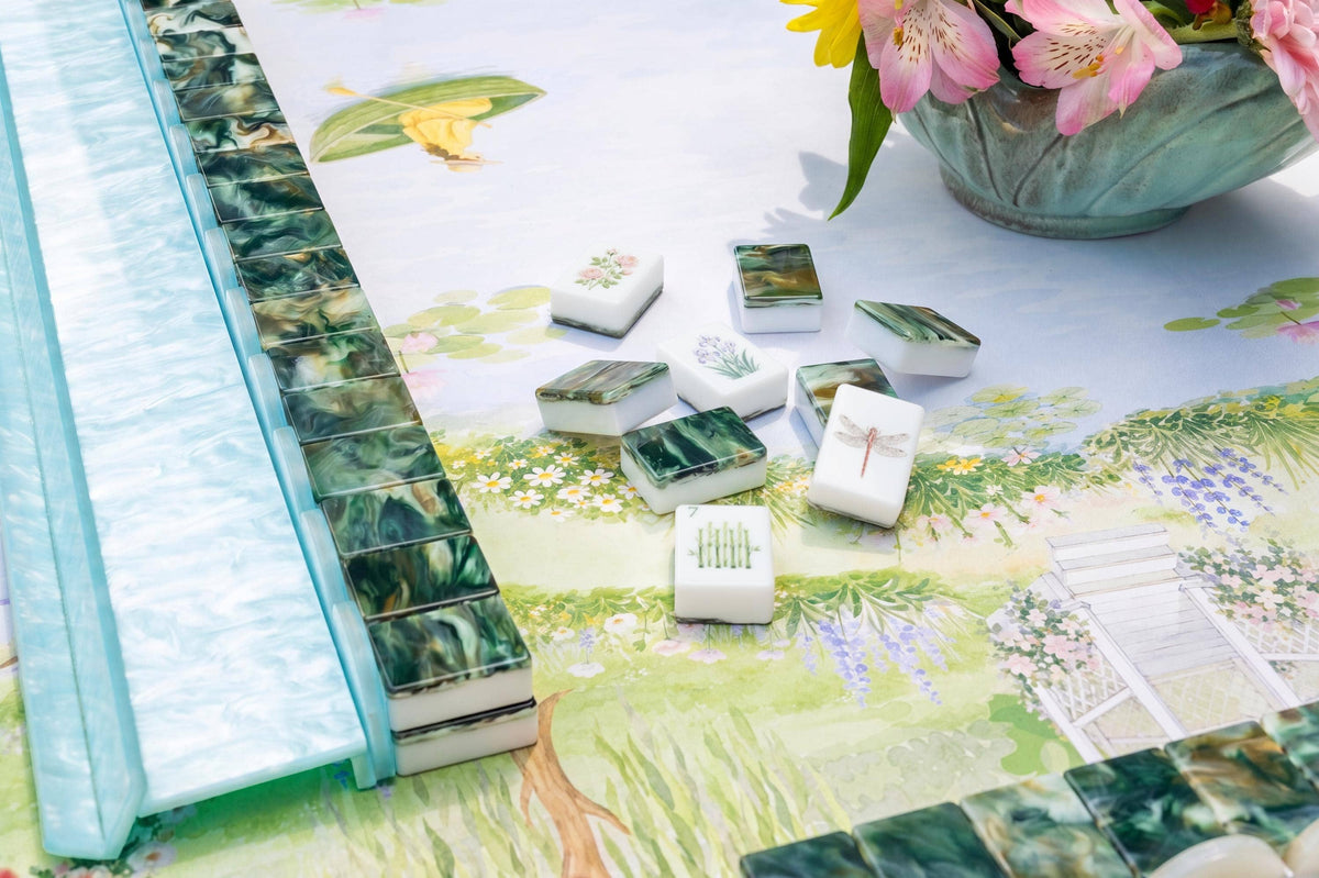 A set of mahjong tiles arranged on a decorative printed mat with a turquoise frame, alongside a matching turquoise rack. The tiles feature a mix of green, white, and multicolor scenic patterns.