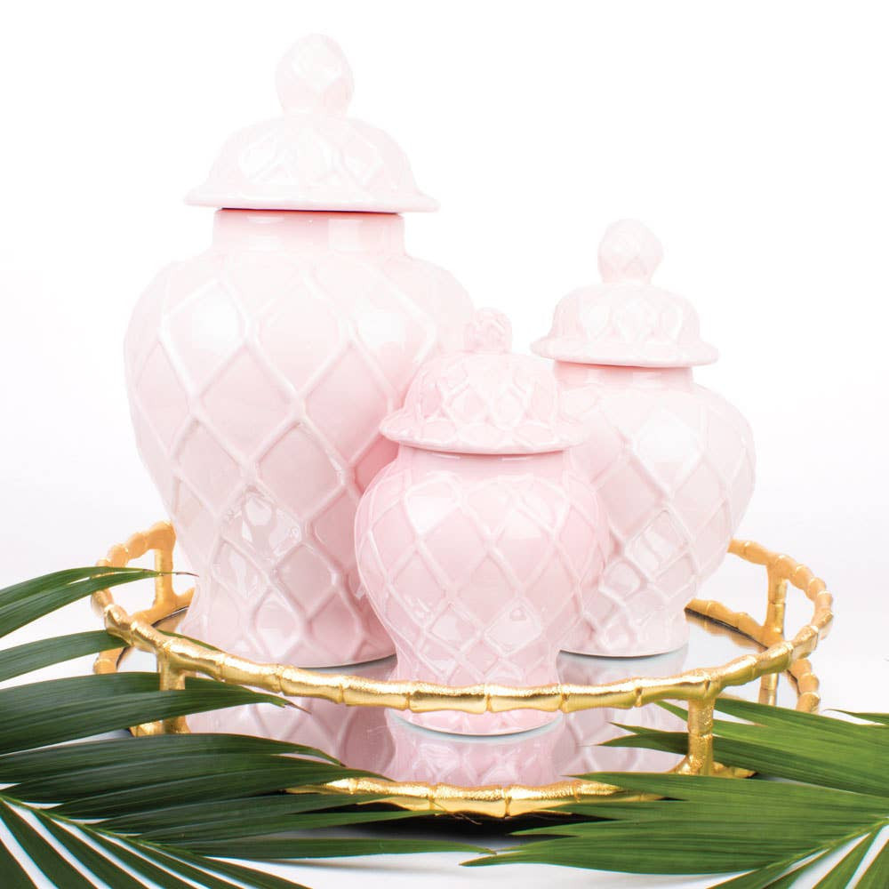 Pink ceramic jars with a gold tray and green leaves on a white background