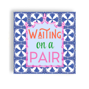 A cocktail napkin that says 'WAITING on a PAIR' in orange, green, and pink lettering on a pale blue center, surrounded by a pink bamboo-style border and a blue-and-white patterned tile-like frame, shown on a white background.