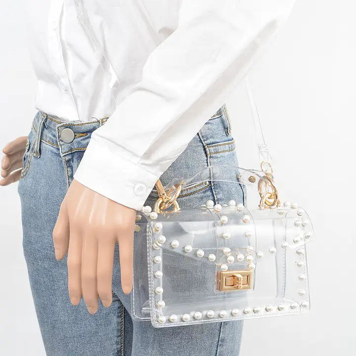 Woman wearing white button-down shirt and jeans carrying transparent pearl-studded clear clutch as a crossbody bag with gold hardware, lifestyle view