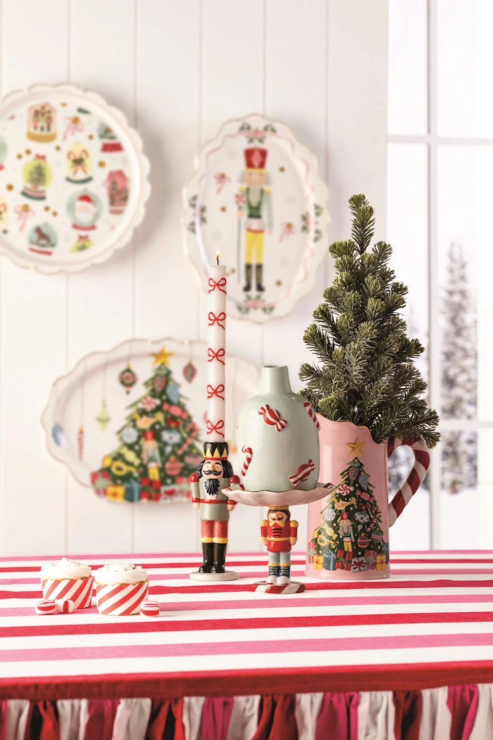 Christmas-themed table setting with decorative plates, vases, and small tree on a red and white striped tablecloth.