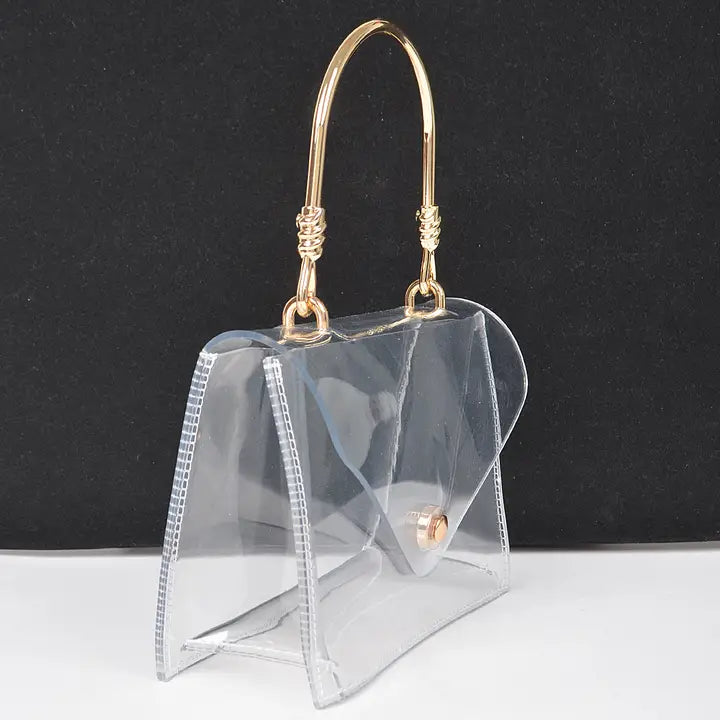 Transparent clear flap clutch with gold metal top handle and gold ball button closure, side profile view on dark background showing bag depth and structure


