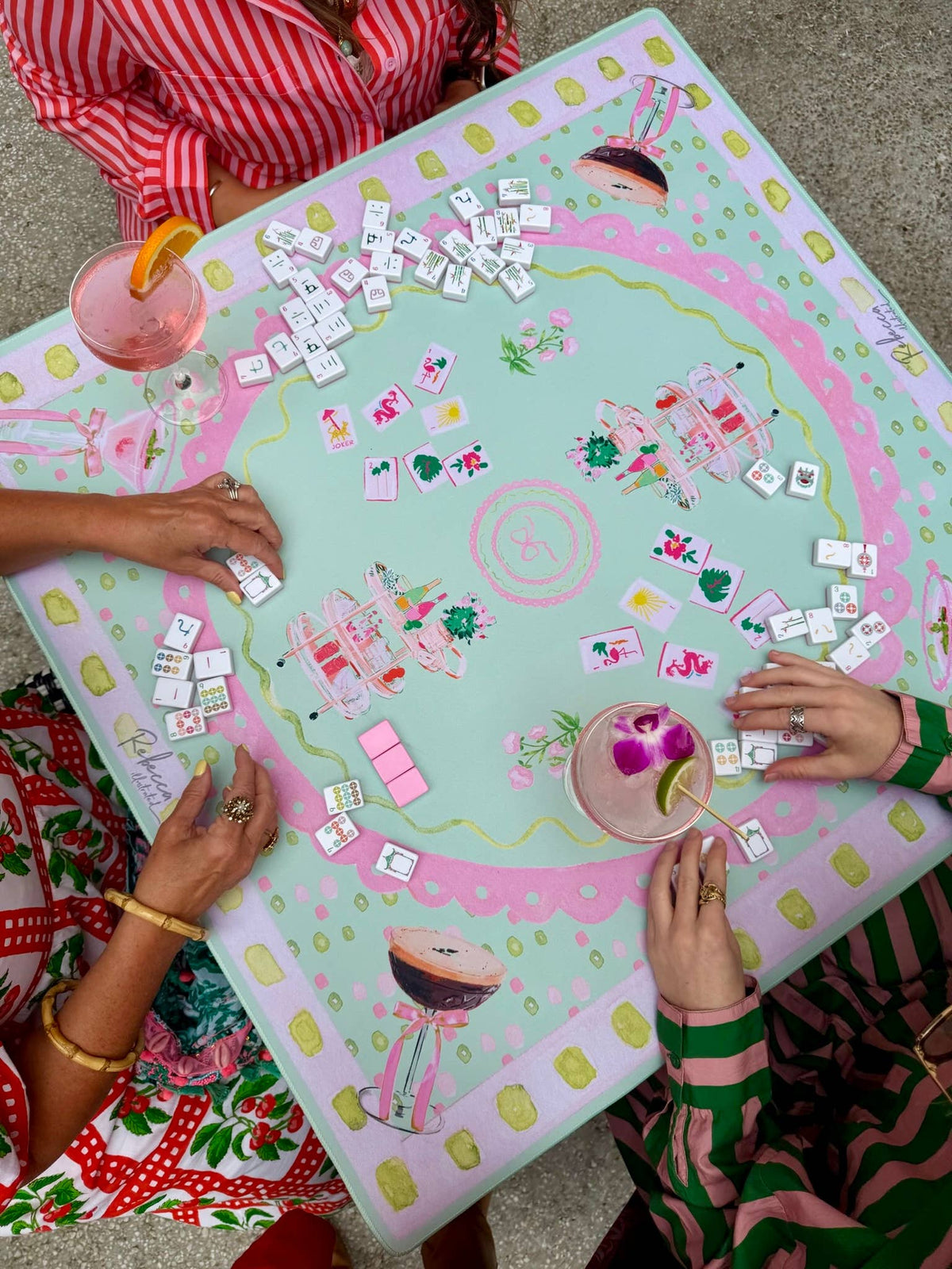 people paying mahjong on a Pink and green illustrated mahjong mat with colorful tile and cocktail cart design 