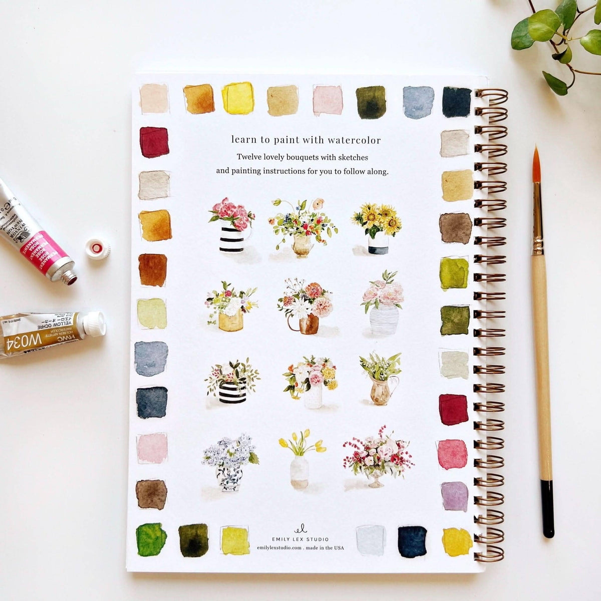 Notebook with watercolor flower designs and painting tools on a white surface