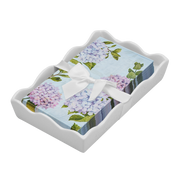 dinner size napkins by Sophistaplate that have hydrangea patternin light blue, lavender and green on a white scalloped tray with white rbbon and bow on a dark background