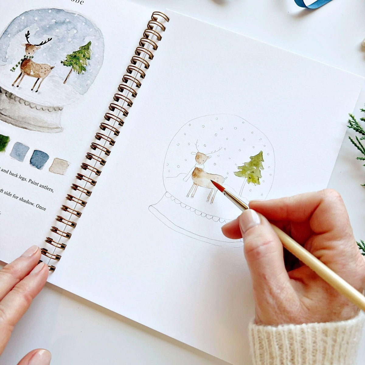 Person coloring a reindeer in a snow globe illustration from a book
