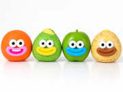 Four cute, cartoonish fruit-shaped squishy, crunchy sensory toys lined up against a white background. From left to right: an orange with a pink smile, a green avocado with a yellow smile, a green apple with a blue smile, and a yellow potato with a brown smile.