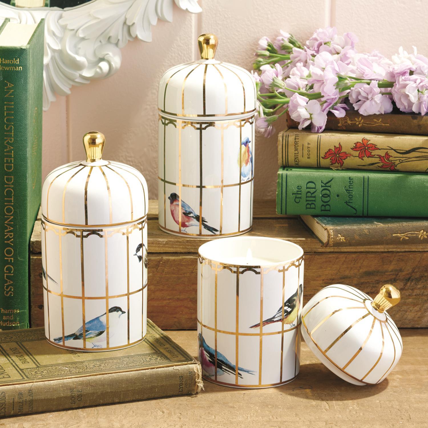 Decorative canisters with bird illustrations on a surface with books and flowers.