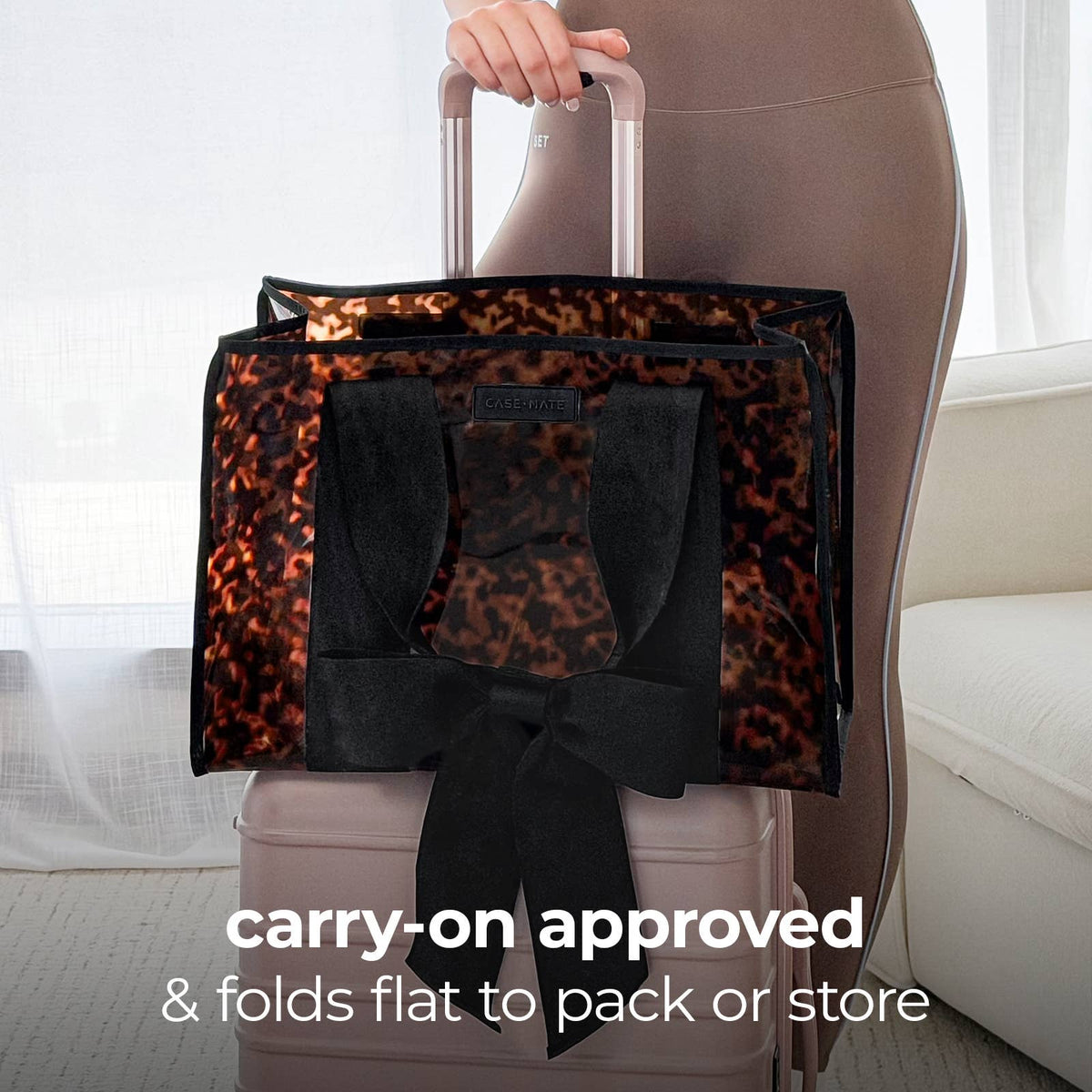 Person holding a folded tortoise shell print and travel bag next to a suitcase with text 'carry-on approved & folds flat to pack or store'.