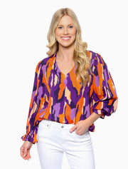 Woman wearing a colorful patterned blouse with white pants on a white background