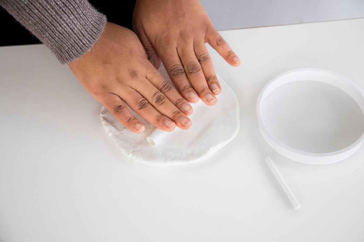 Hands pressing a white object on a white surface with a white container in the background.