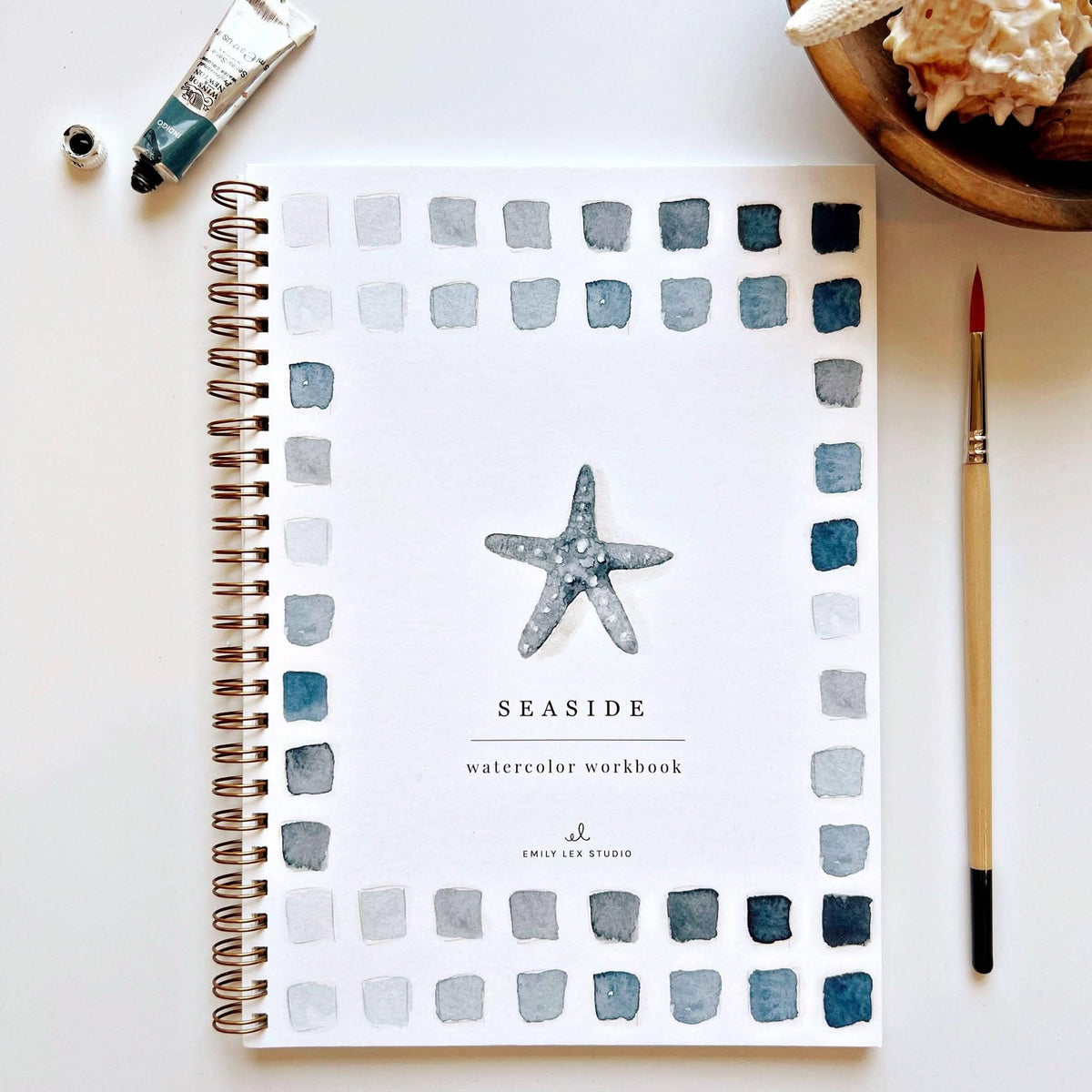 Seaside watercolor workbook with starfish design on a white surface with art supplies.