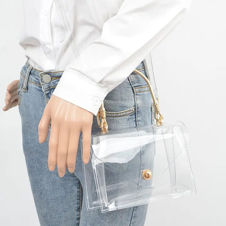 Woman in white button-down shirt and jeans carrying transparent clear flap clutch with gold metal handle at her side, lifestyle view showing wearable size