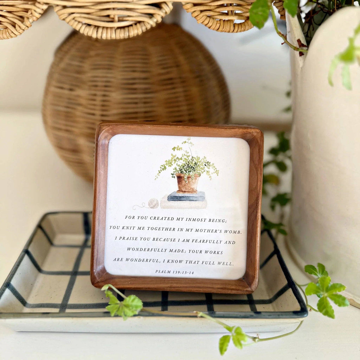 Decorative wooden frame with a plant illustration and text on a shelf with decorative items.