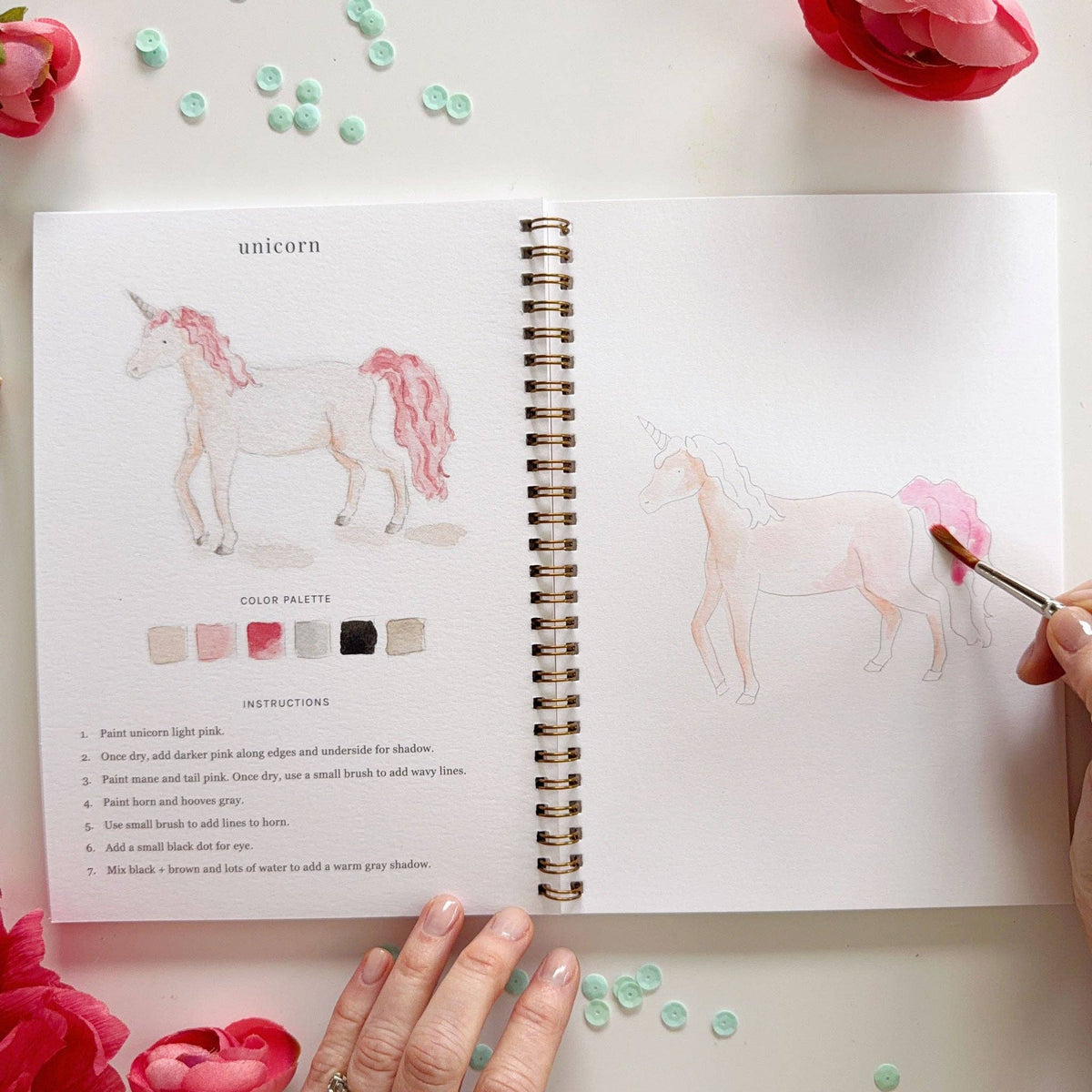 Open book with unicorn watercolor  illustration and color palette, surrounded by flowers.