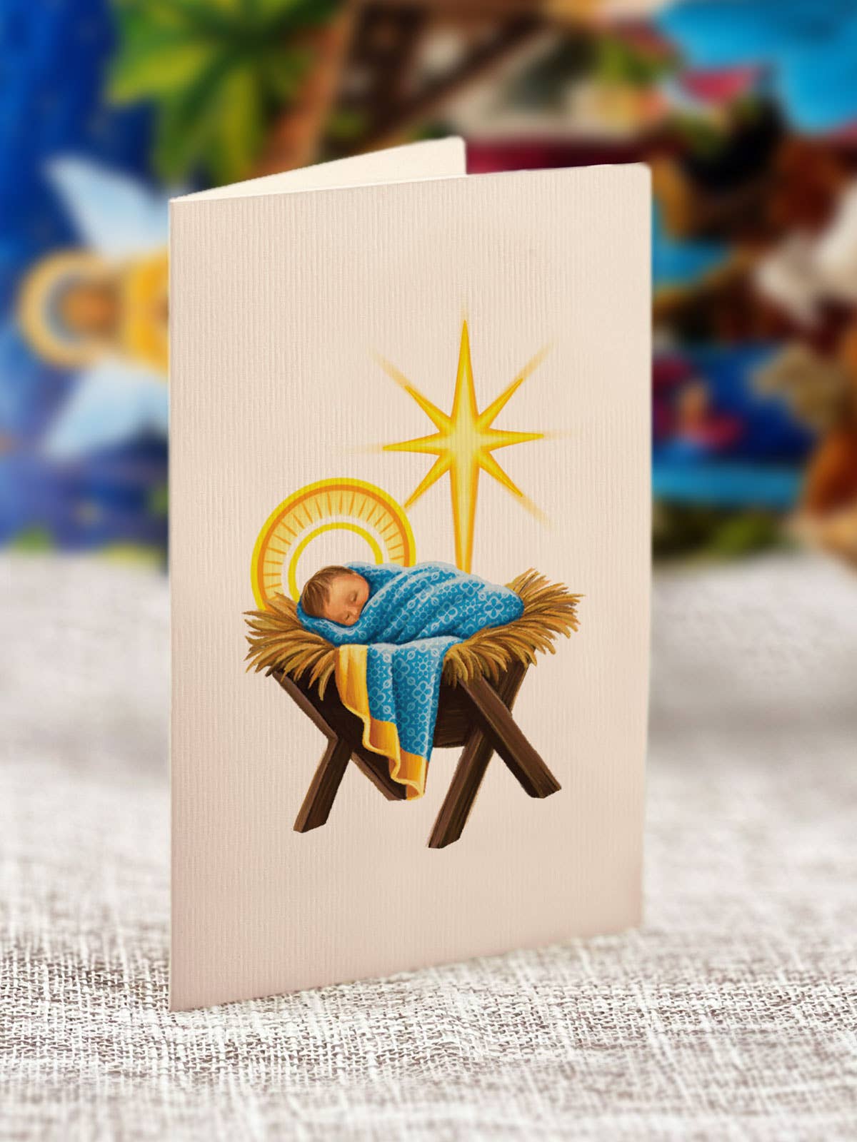 Card with illustration of baby Jesus in a manger on a textured surface with a colorful background.