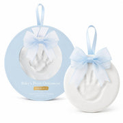 A baby footprint keepsake ornament shown both inside its round light blue presentation box and as the free ornament beside it. The ornament is white with a pale blue ribbon bow and hanging loop, and the box reads 'Baby's Print Ornament' with 'keep & mine' below.