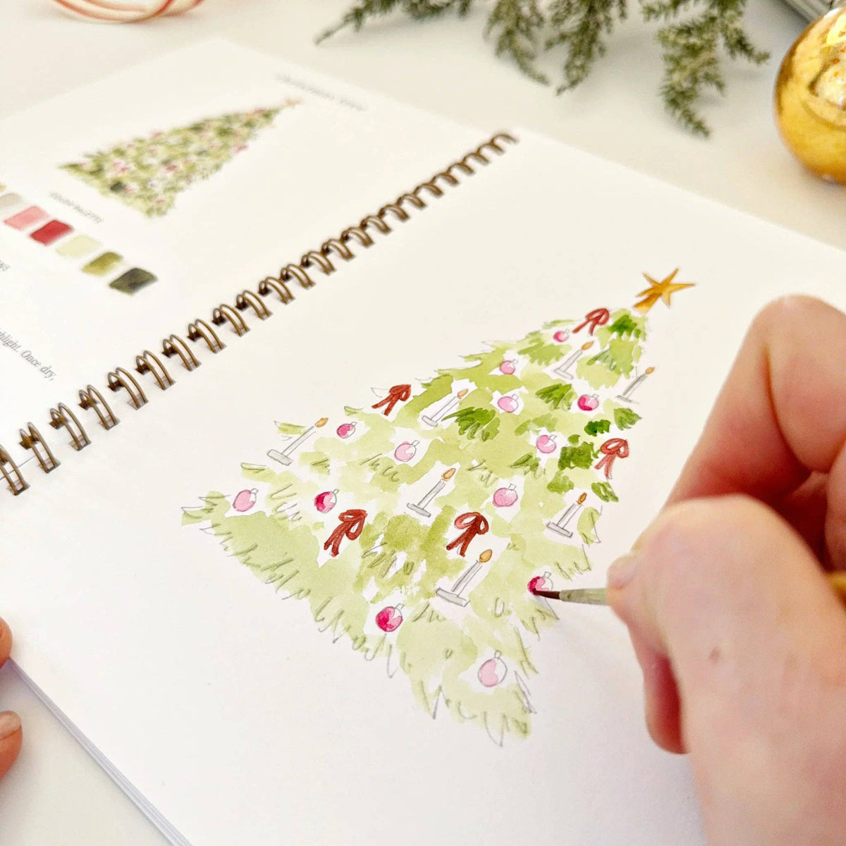 Person painting a Christmas tree on a spiral-bound notebook.