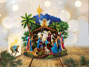 Freshcut Paper pop-up card Nativity scene with characters and animals on a wooden platform with a blurred light background