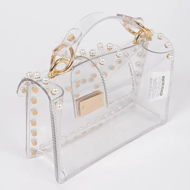 Transparent clear clutch bag with faux pearl trim and gold ring hardware, side angle view showing depth and structured shape on white background