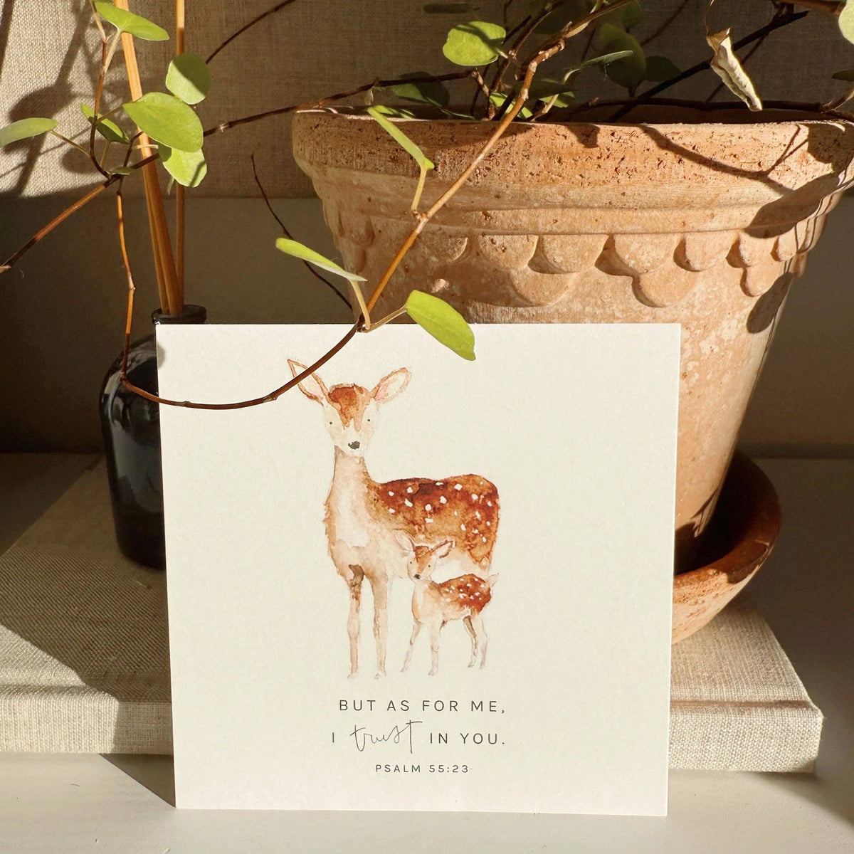Card with deer illustration and scriptural text on a surface with a plant in the background
