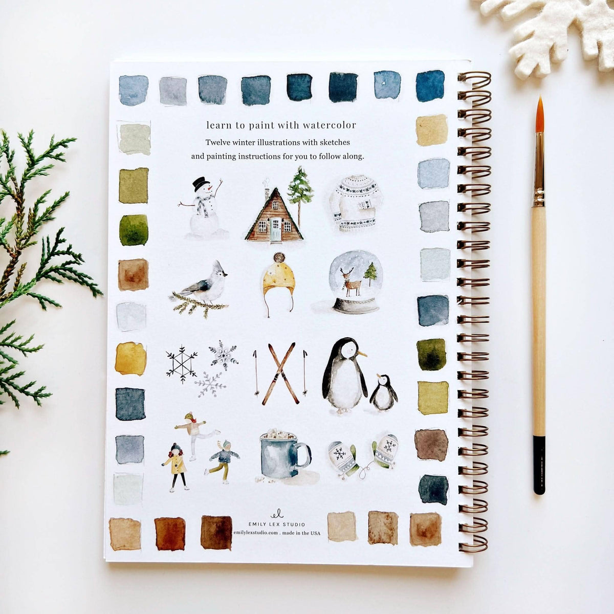 Illustrated notebook with winter-themed illustrations on a white surface with a paintbrush.