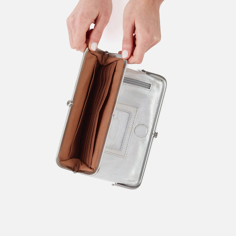 Hand holding a silver clutch with brown interior on a white background