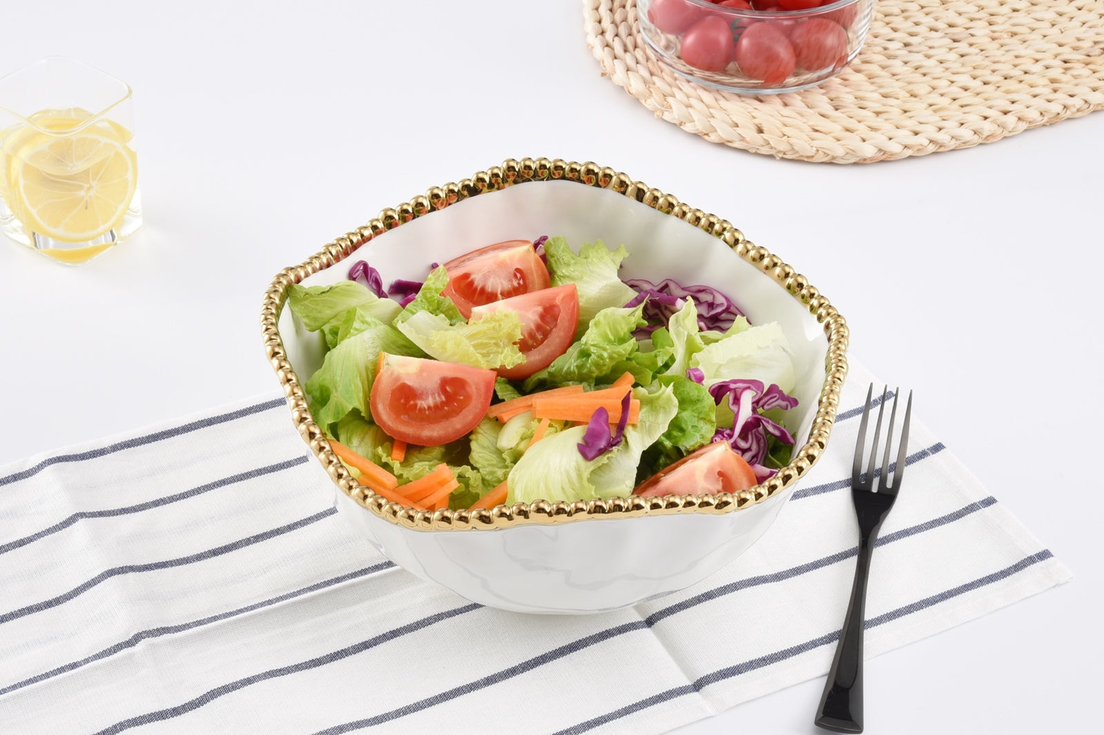 Salad in a decorative bowl on a table with a fork and lemon wedge.