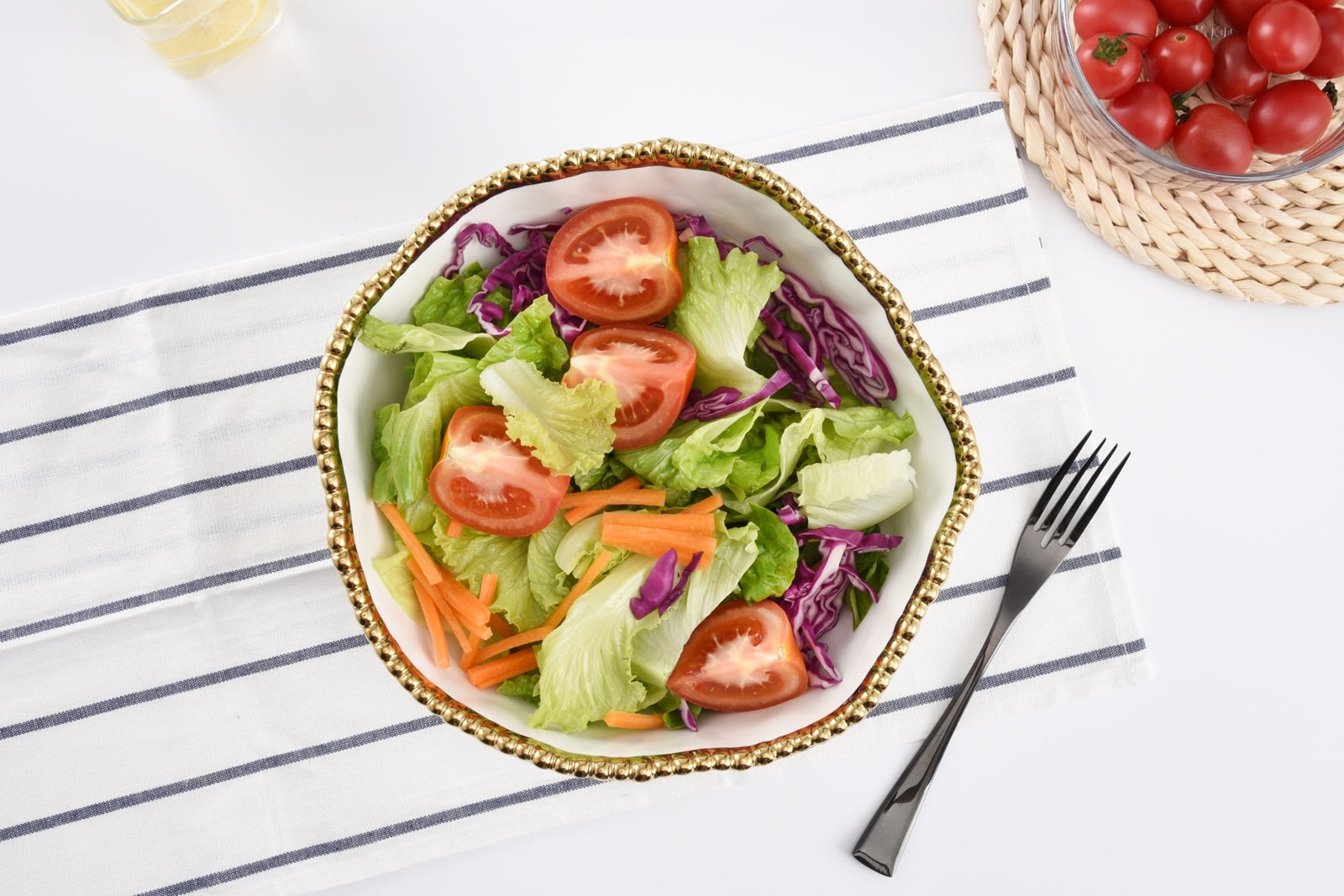Colorful salad with tomatoes, lettuce, and carrots in a bowl on a striped tablecloth.