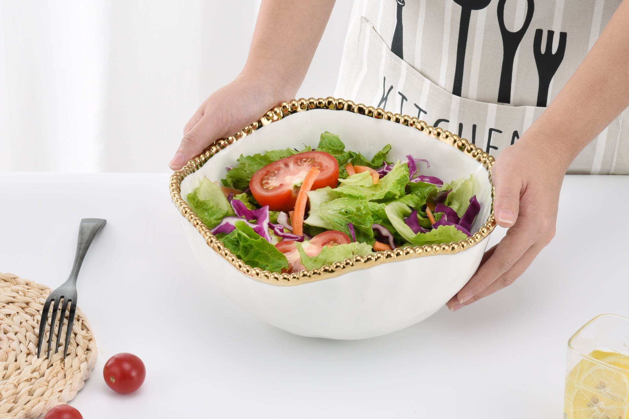 Person holding a bowl of salad on a white surface with a kitchen apron in the background.