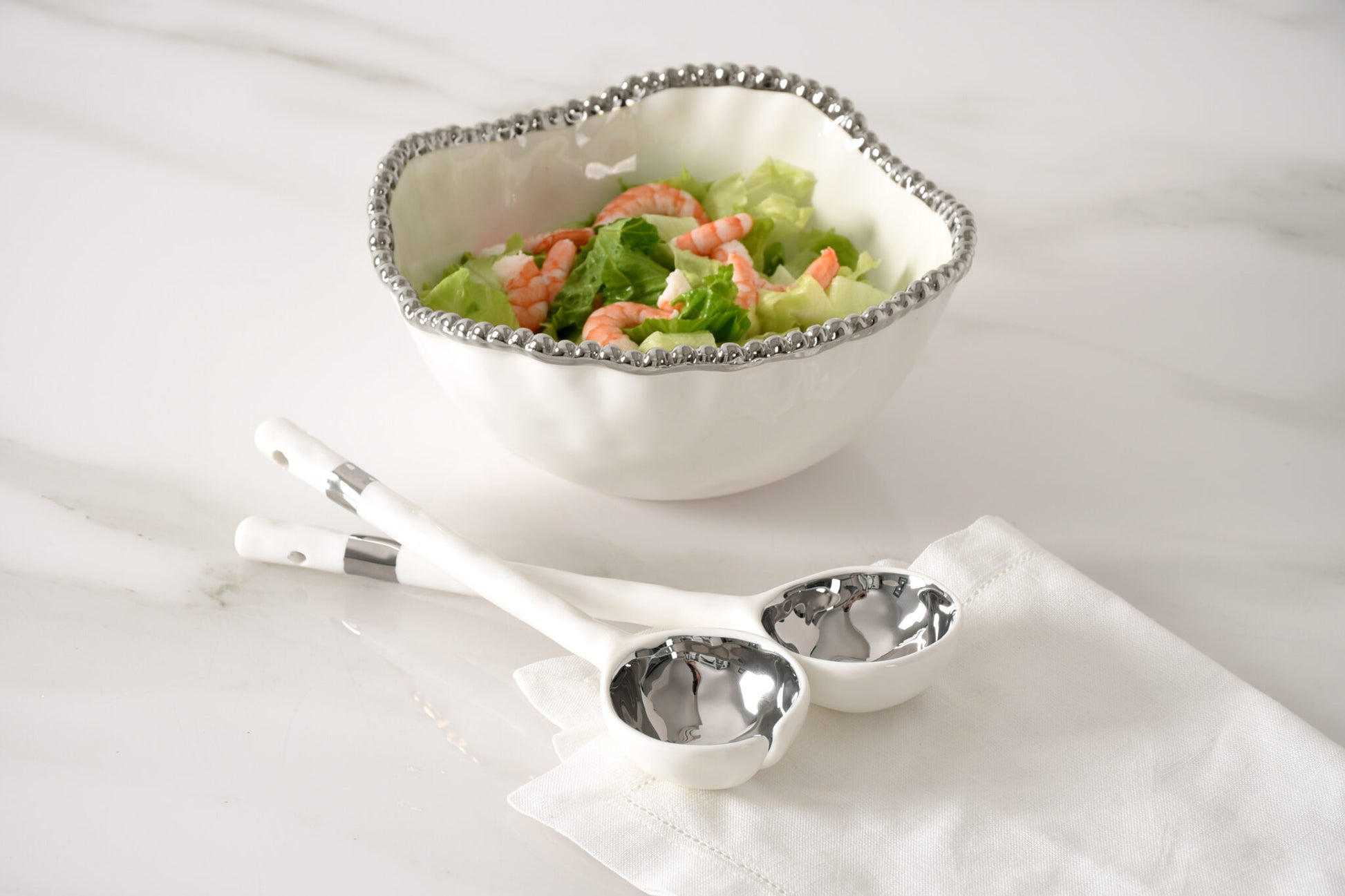 Bowl of salad with serving spoons on a white surface