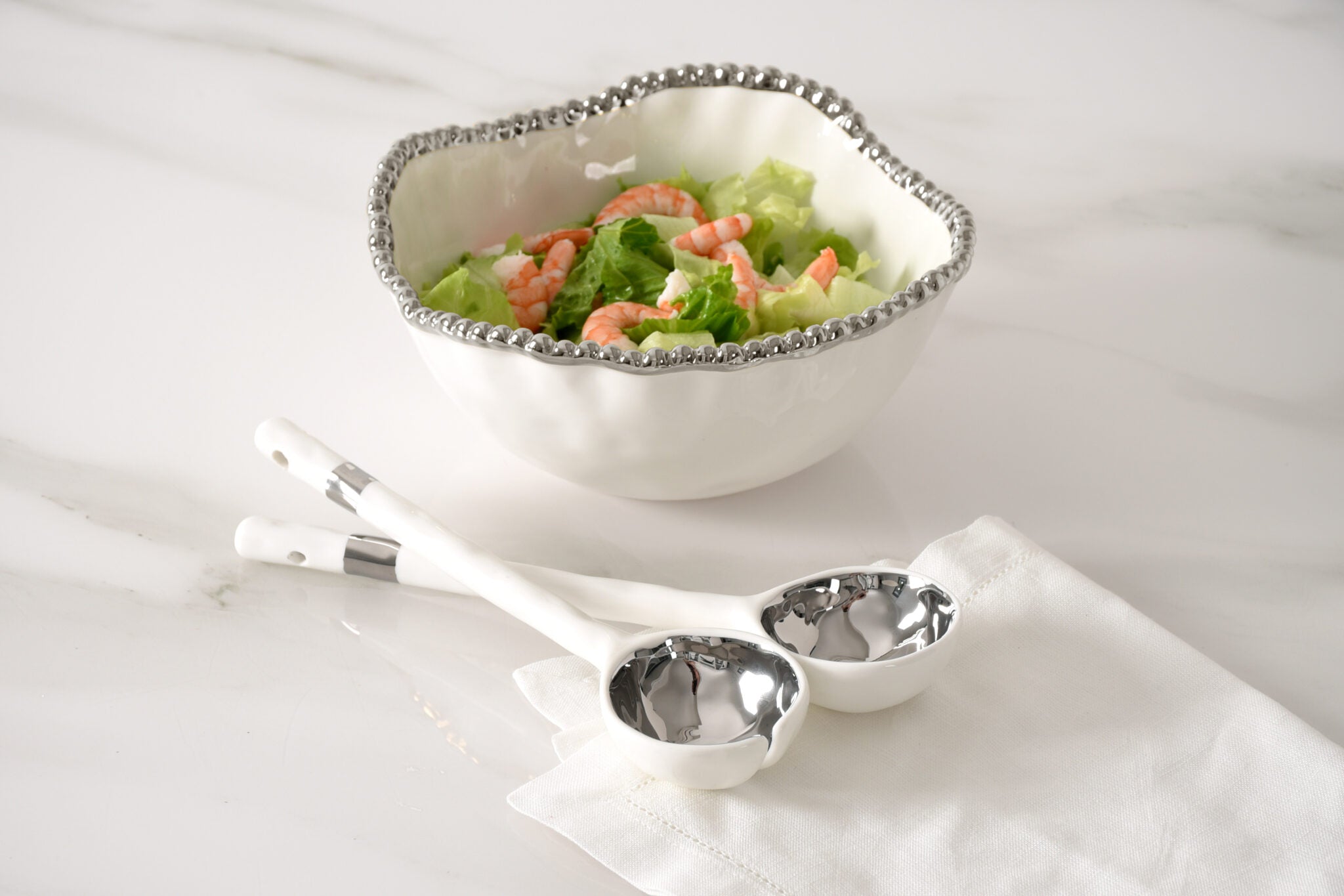 Bowl of salad with serving spoons on a white surface