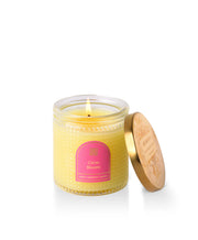 Yellow candle in a glass jar with a pink label on a white background