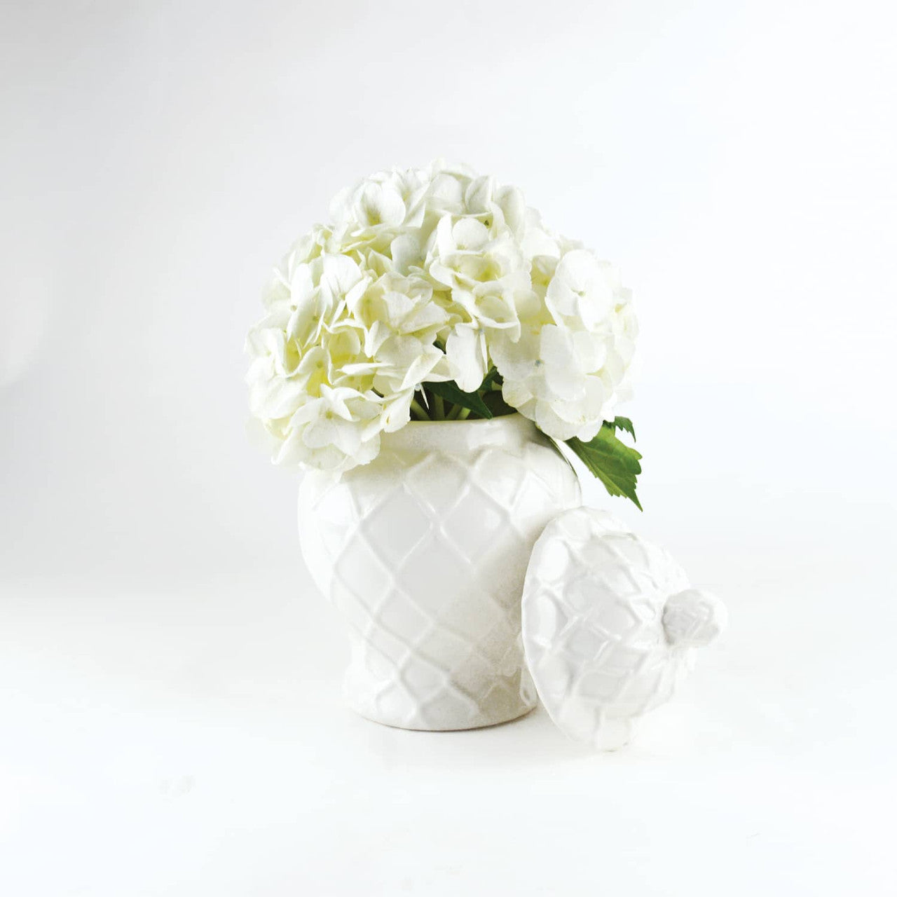 White geometric-patterned 8 Oak Lane Brand White ceramic Ginger jars with white flowers on a marble surface vase with a lid on a light gray background