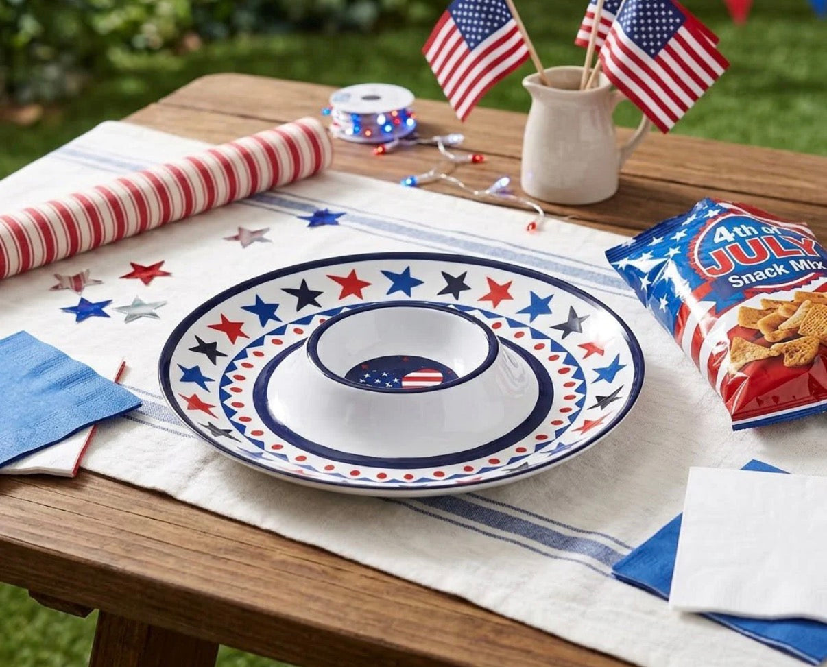 Table setting with a decorative plate, American flags, and snack mix on a wooden table outdoors.