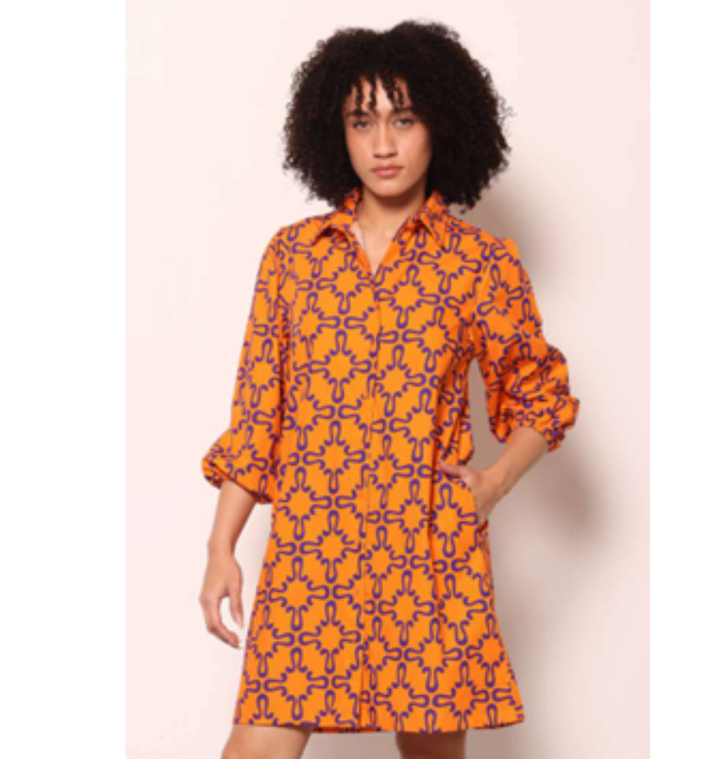 Woman wearing an orange and purple patterned dress against a plain background
