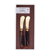 Two gold spreaders with tortoiseshell handles in a Two's Company packaging on a white background